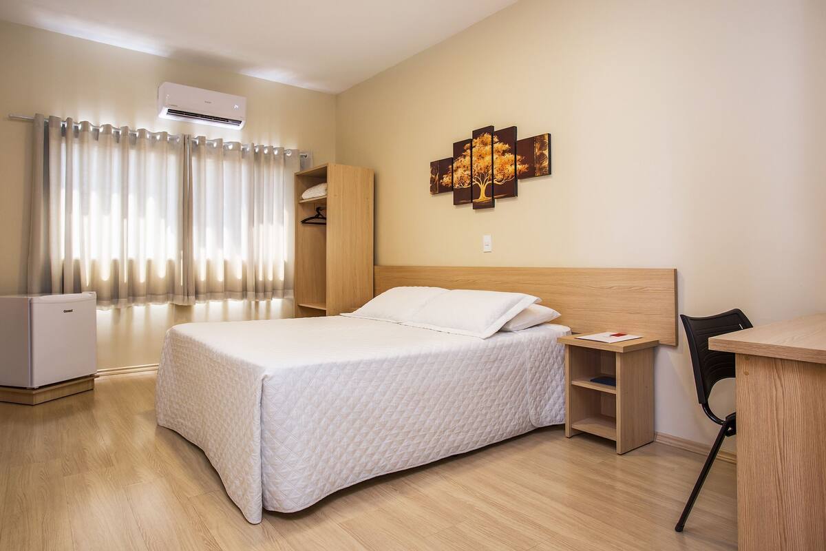 Ett hotellrum med en säng, ett skrivbord, en stol, en luftkonditionering och en garderob.