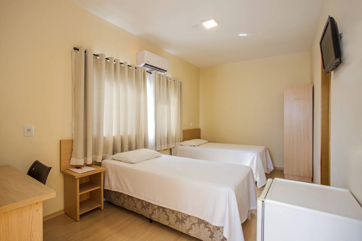 Ett hotellrum med två sängar, ett skrivbord, en stol, en luftkonditioneringsanläggning och en tv.
