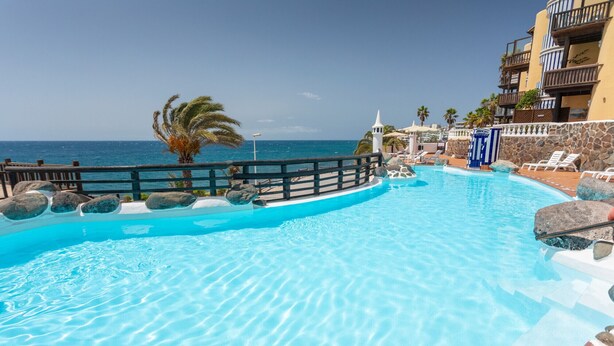 A clear blue pool with a wooden deck and lounge chairs, overlooking the ocean.