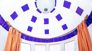 A corner seating area with a round table, orange cushions, and a bowl of fruit.