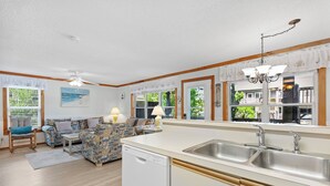 Et moderne køkken med en stor ø, et spiseområde med sofa og bord, samt store vinduer med gardiner.