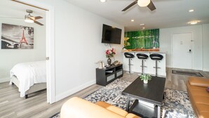 A modern living room with a sofa, a dining table, and a kitchen area with a TV and bar stools.