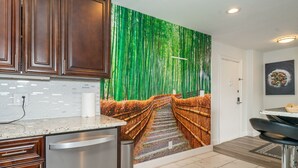 A kitchen with wooden cabinets, a stainless steel dishwasher, a bamboo-themed mural, and a bar area with a white countertop.