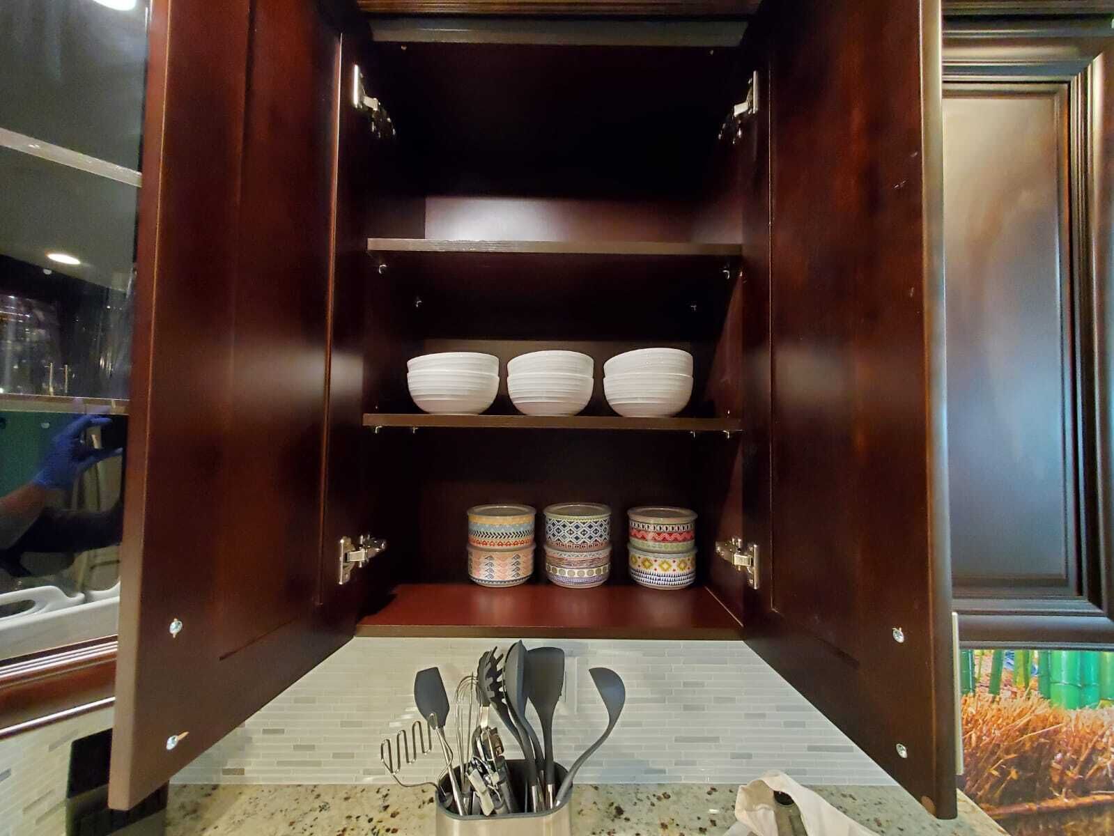 Un meuble de cuisine avec des étagères où sont rangés des bols blancs et des récipients à motifs.