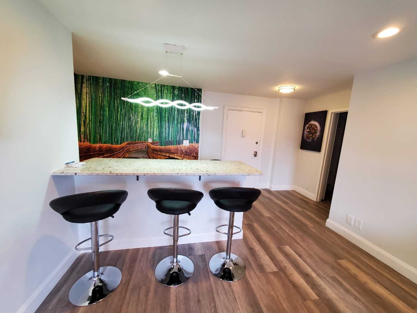 Une cuisine moderne dotée d’un îlot central, de trois tabourets de bar et d’une fresque murale décorative.