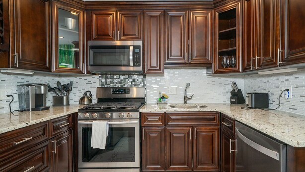 A modern kitchen with dark wood cabinets, stainless steel appliances, and a tiled backsplash.