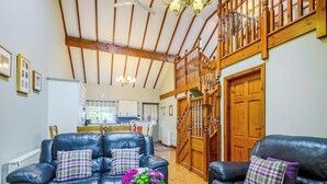 Ein geräumiges Wohnzimmer mit zwei Ledersofas, einem Holztisch und einem Blumenvasen. Eine Holzt Treppe mit Geländer führt zu einer oberen Ebene.