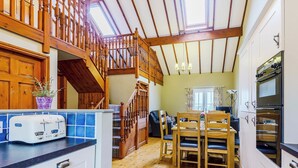 Eine geräumige Küche mit Holzböden, eine Essecke mit Tisch und Stühlen, eine Treppe und ein Blick ins Freie durch ein Oberlicht.