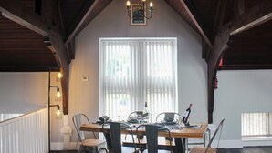 Zona pranzo con tavolo in legno, sedie, un lampadario e una finestra con persiane.