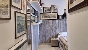 A narrow hallway with a radiator, a bed, and a shelf with framed pictures. - Guest house Biffi Simone (Florence)