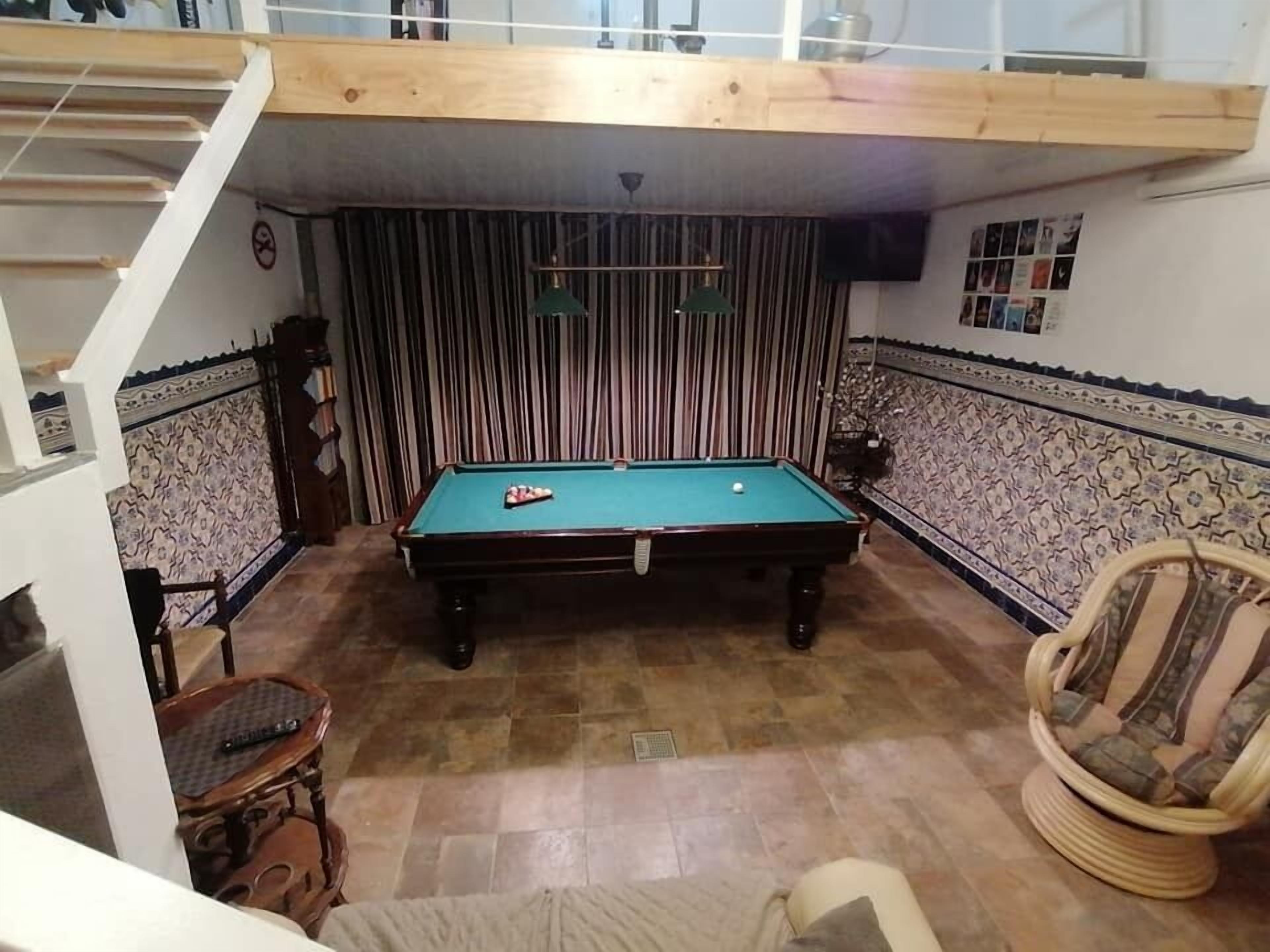 A pool table in a room with patterned tile walls, a wooden ceiling, and a chair with a cushion.