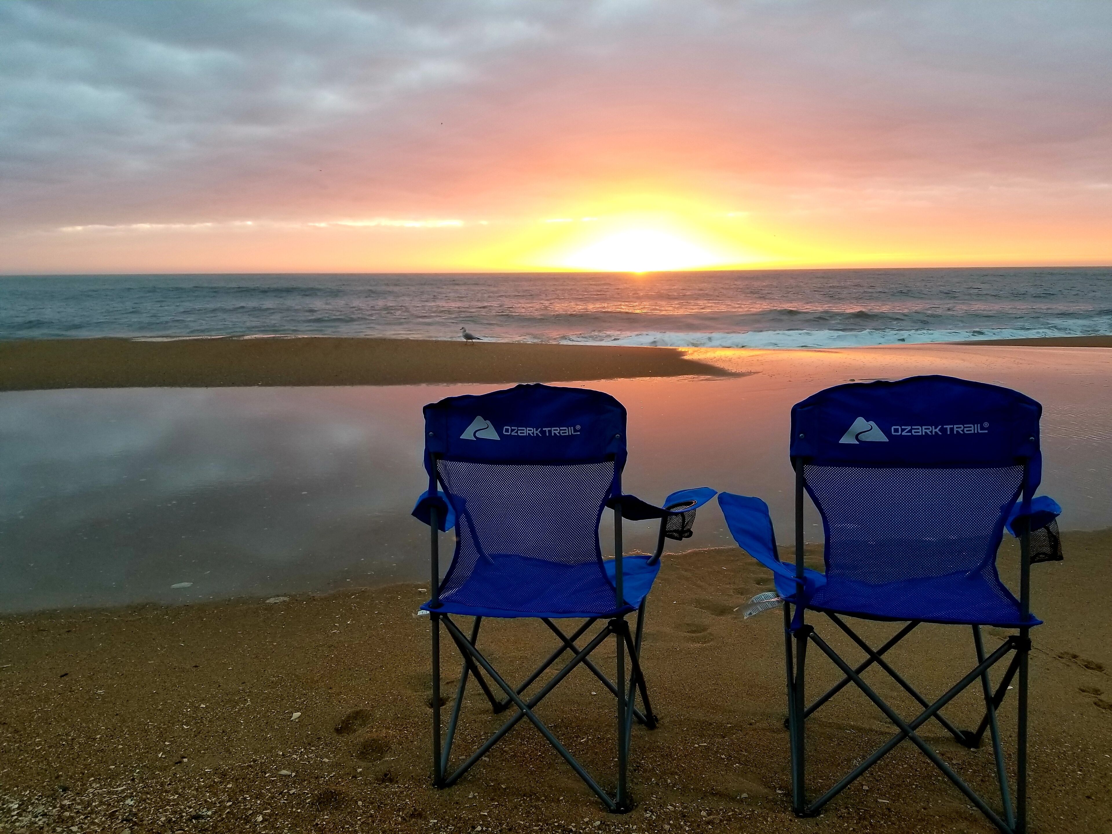 Deux chaises de plage bleues de la marque Ozark Trail, placées face à l’océan au coucher du soleil.