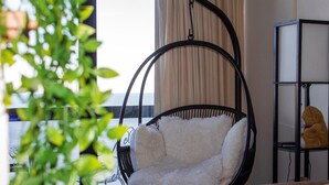 Um quarto com uma cadeira suspensa, estante e janela com cortinas.