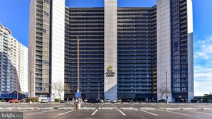 Um hotel moderno com um logotipo vertical destacado, vários andares e um estacionamento à frente.