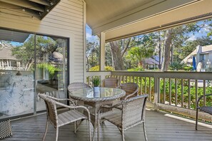 A covered patio with wicker furniture and a glass table, overlooking a residential area with trees and houses. - Gorgeous Vacation Villa w/ Community Pool (Hilton Head Island)