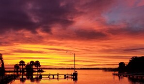 Ein Sonnenuntergang über ruhigem Wasser mit einem Steg und Bäumen.