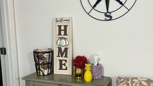 Un meuble décoratif surmonté d’une pancarte indiquant « Bienvenue chez vous », d’une boussole et de divers objets.