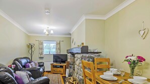 A living room with a sofa, TV, fireplace, dining table set with plates and glasses, and a vase of flowers. - 2 bedroom accommodation in Caethro, near Caernarfon (Caethro, near Caernarfon)