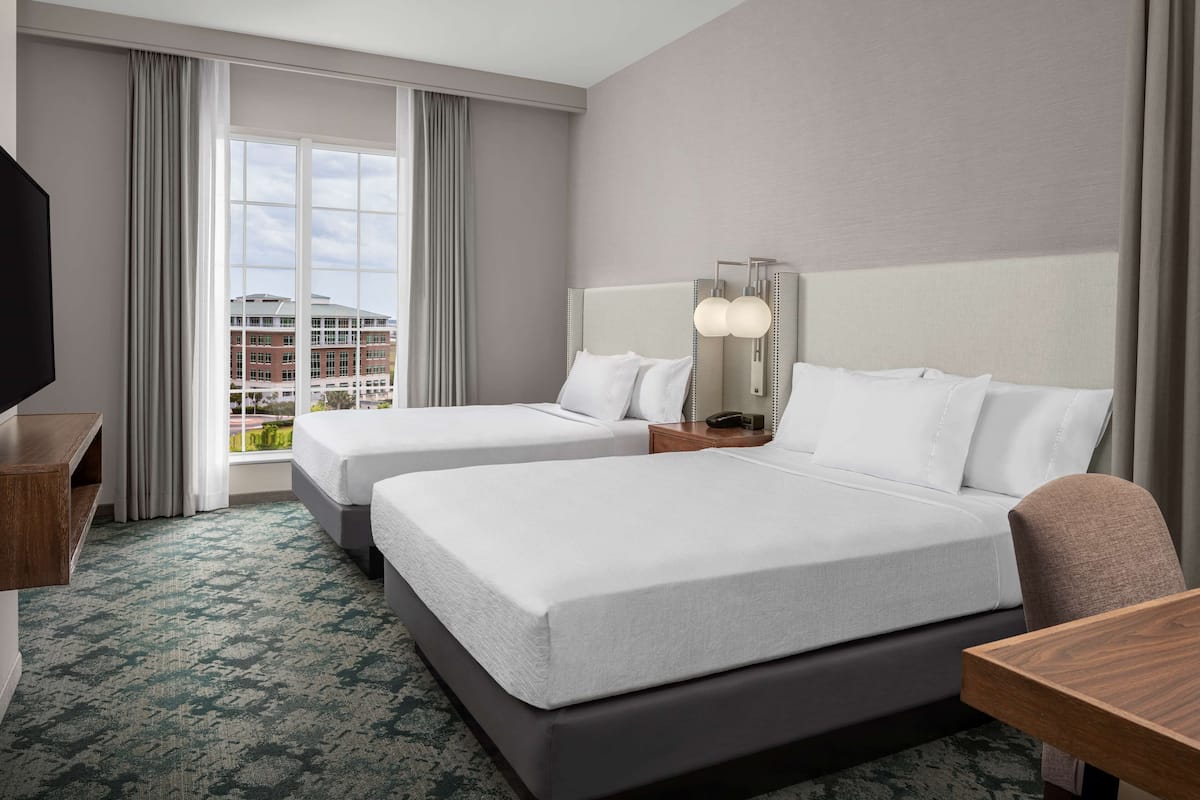 Une chambre d’hôtel avec deux lits, un bureau, une télévision et une grande fenêtre avec des rideaux.