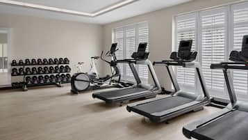 Een fitnessruimte met loopbanden, een hometrainer en een rek met gewichten.