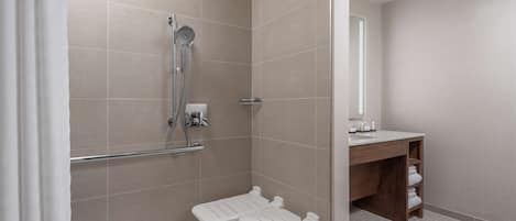 A modern bathroom with a shower, a toilet with a grab bar, a sink, and a mirror.