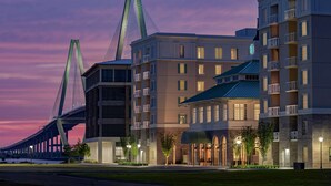 A modern hotel with a prominent bridge in the background, featuring multiple floors and balconies. - Embassy Suites by Hilton Charleston Harbor Mt. Pleasant (Mount Pleasant)