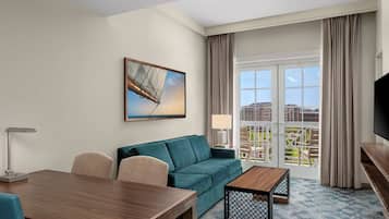 A hotel room with a sofa, a wooden table, a TV, and a balcony with a city view.