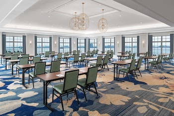 A swimming pool with lounge chairs and umbrellas, surrounded by brick buildings with large windows and palm trees. at Embassy Suites by Hilton Charleston Harbor Mt. Pleasant