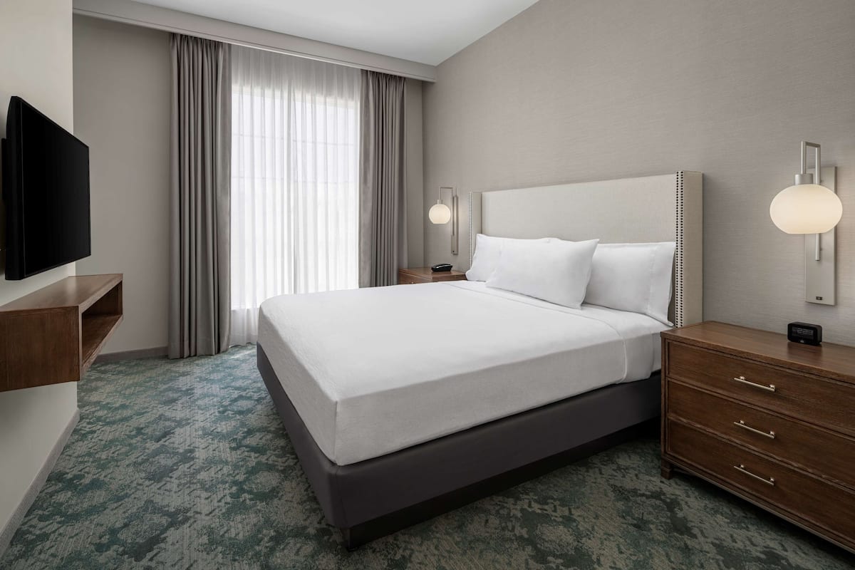 Une chambre d’hôtel avec un grand lit, une télévision, une table de chevet, une lampe et une fenêtre avec des rideaux.