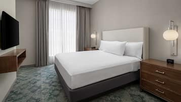 Ein Hotelzimmer mit einem großen Bett, einem Fernseher, einem Nachttisch, einer Lampe und einem Fenster mit Vorhängen.