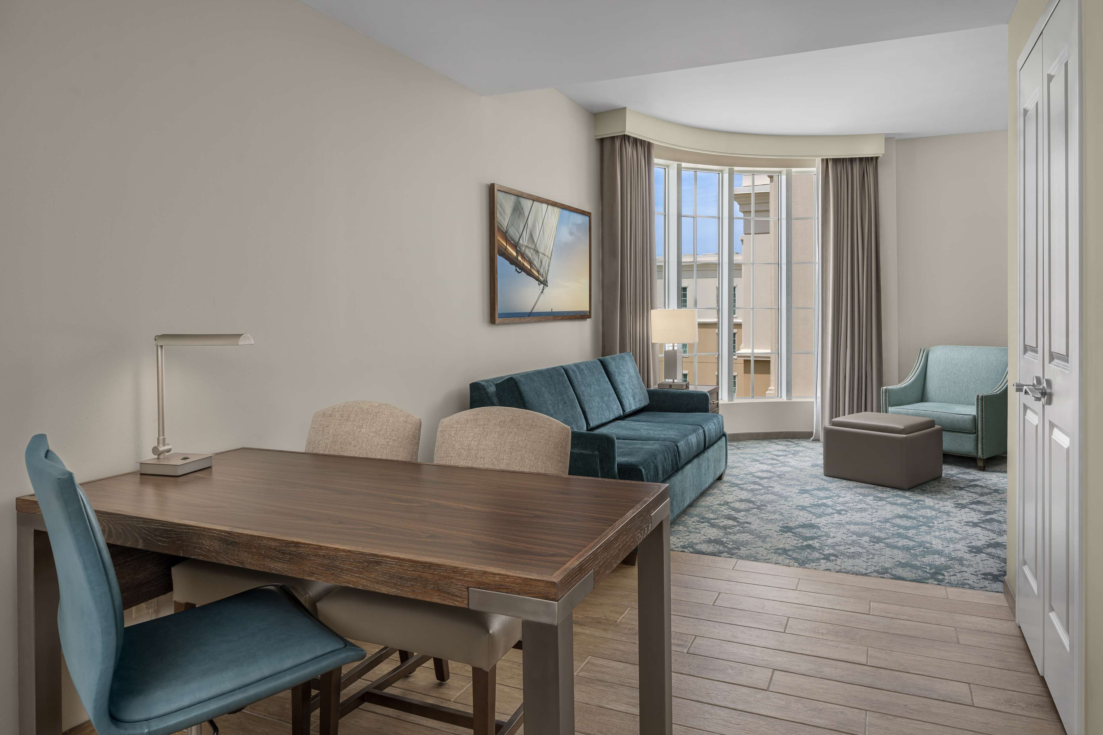 Habitación de hotel moderna con zona de comedor, sofá, una mesita y vistas a la ciudad.