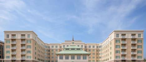 Un hotel grande de varios pisos con un edificio central con techo verde, rodeado por un césped bien cuidado y fachada de ladrillo.