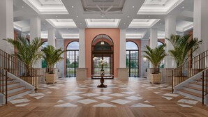 A spacious lobby with a herringbone-patterned floor, a central arched doorway, and potted plants on either side of the staircase. - Embassy Suites by Hilton Charleston Harbor Mt. Pleasant (Mount Pleasant)