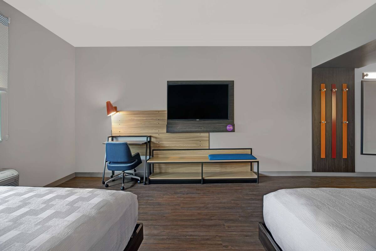 A hotel room with two beds, a desk with a chair, a flat-screen TV mounted on the wall, and a wooden cabinet.