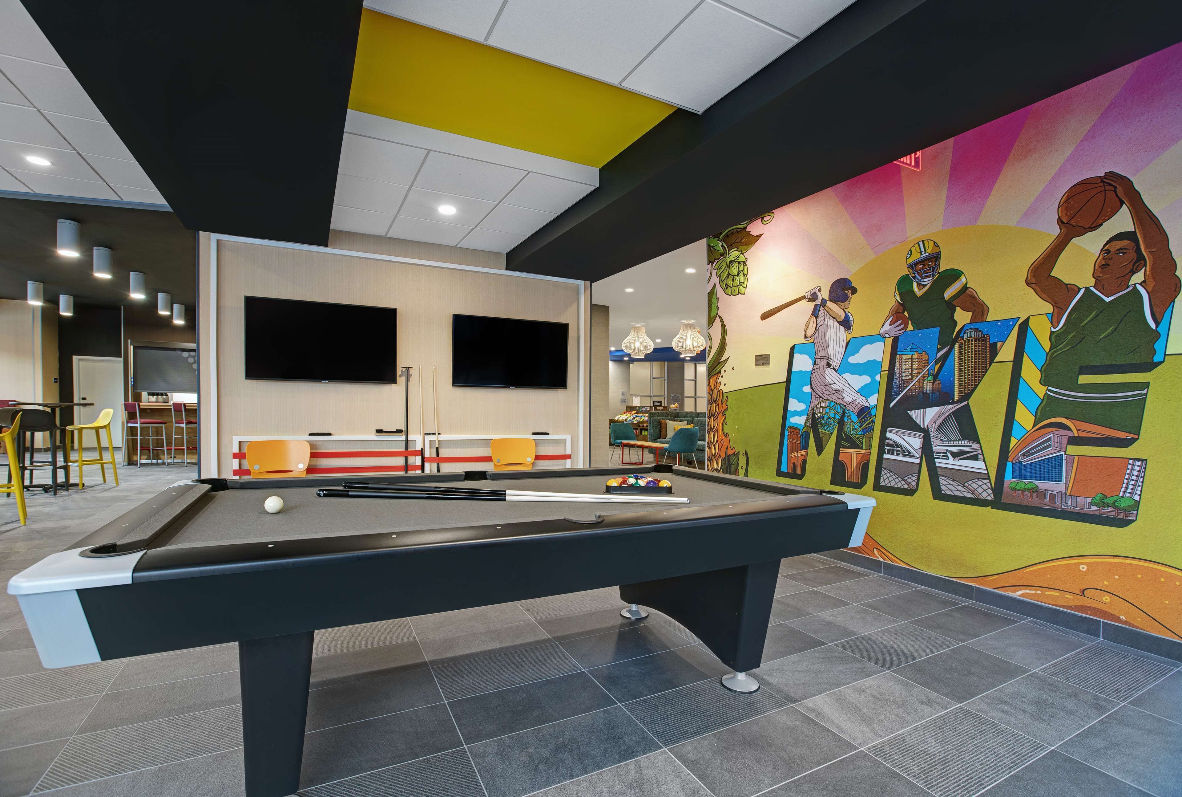 A pool table in a room with a mural, a flat-screen TV, and a seating area with chairs.