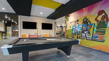 A pool table in a room with a mural, a flat-screen TV, and a seating area with chairs.