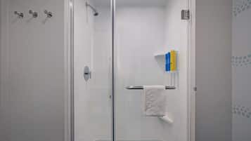 A glass-enclosed shower with a white towel on a rack, a showerhead, and a small shelf with toiletries.