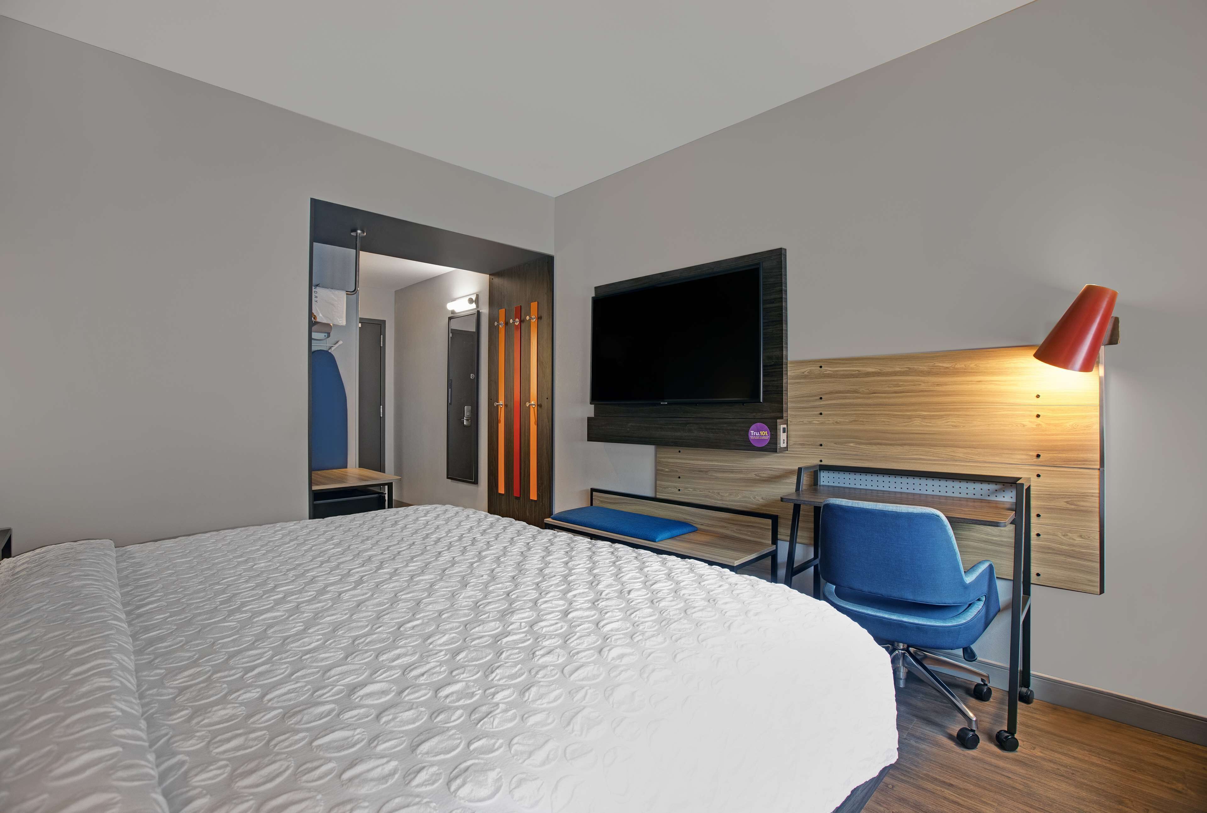 Ett modernt hotellrum med en stor säng, ett skrivbord med en stol, en platt-TV som är monterad på väggen och en röd skrivbordslampa.