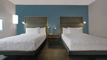 A hotel room with two beds, a nightstand, and a lamp between the beds.