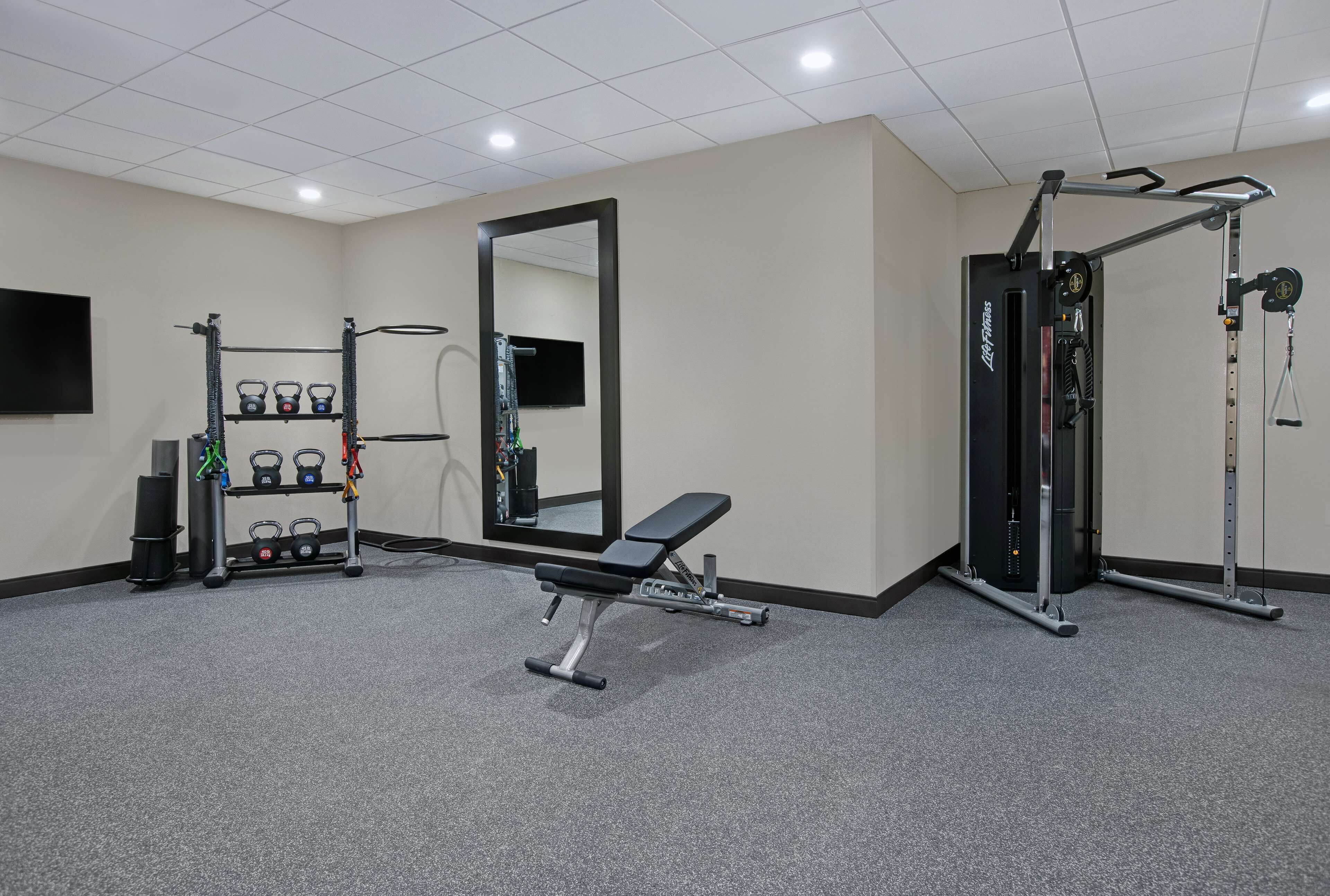 Ett gym med en bänk, kettlebells, ett knäböjsställ och en spegel.