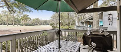 A covered outdoor seating area with a table and chairs, a green umbrella, and a barbecue grill.