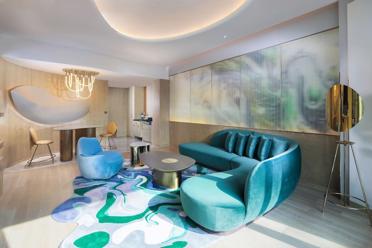 A modern living room with a teal sofa, a round coffee table, and a unique abstract rug.