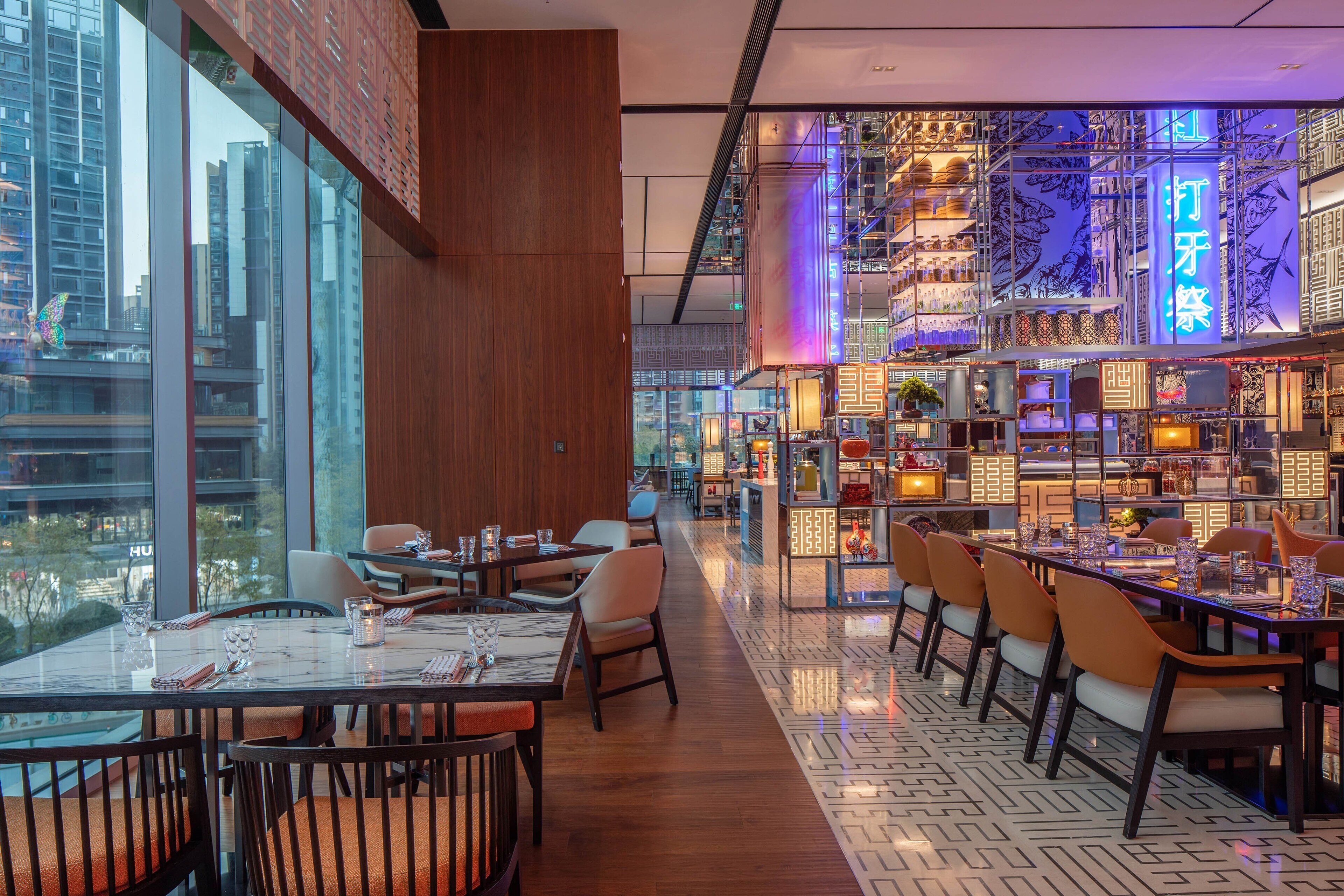 Um restaurante moderno com tetos altos, amplas janelas e vista para a paisagem urbana.