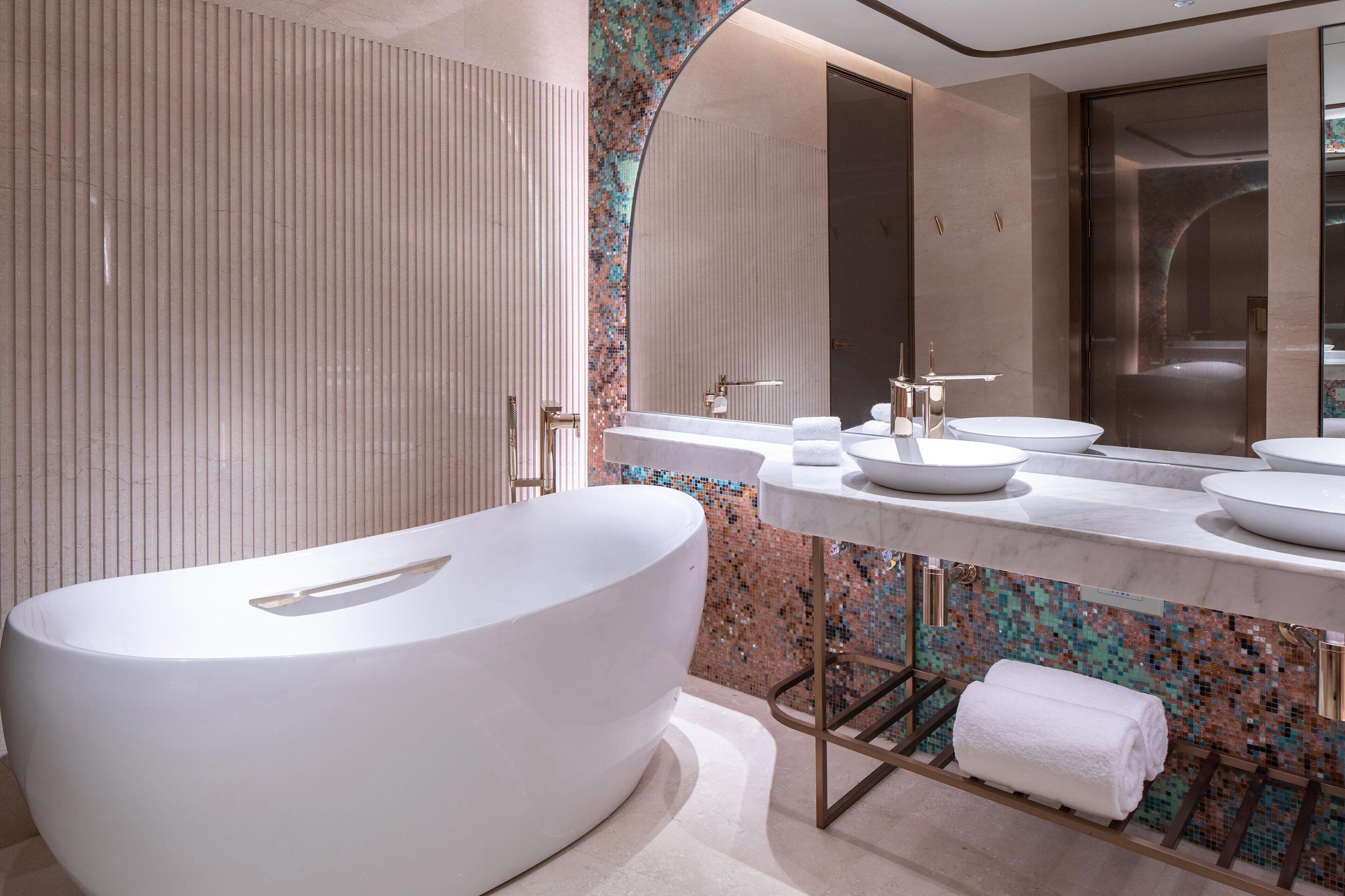 A modern bathroom with a freestanding bathtub, a large mirror, and a tiled backsplash.