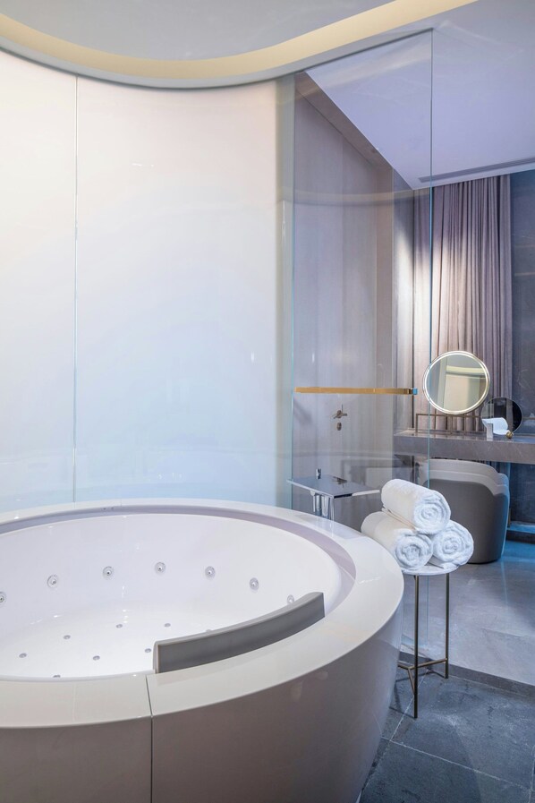 Un baño moderno con una bañera circular grande, un tocador con espejo y toallas ordenadas.