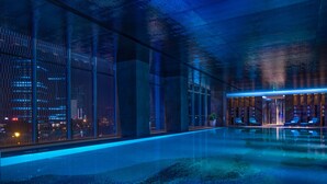 Un área de piscina interior moderna con paredes de vidrio, una piscina cristalina y sillones de descanso.