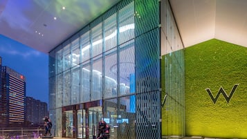 Een modern gebouw met een glazen gevel en een groene, structuurrijke muur met een groot 'W'-logo.