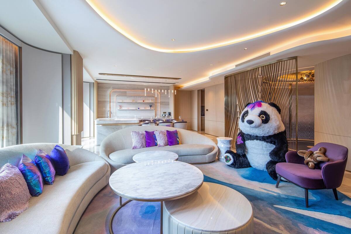 A modern living room with a large panda statue, a sofa, a coffee table, and a purple armchair.