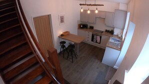 A kitchen with wooden cabinets, a wooden table, and stools. There is a staircase leading to another level. - Albert Cottage, Skipton (Skipton)