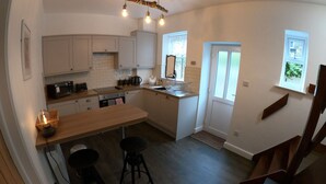 A modern kitchen with white cabinets, a wooden countertop, and a dining area with stools. - Albert Cottage, Skipton (Skipton)